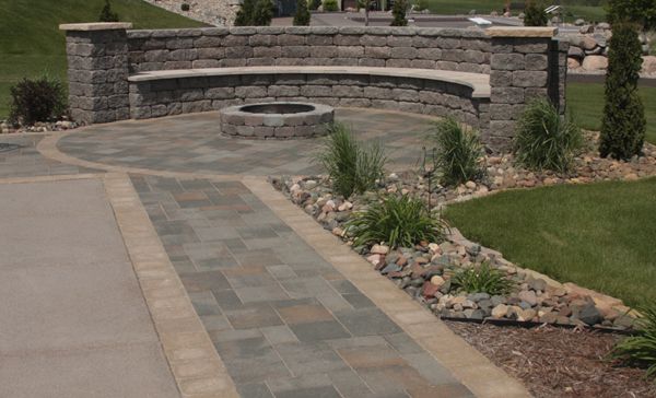 A cozy gathering spot uses VERSA-LOK retaining wall units, in the Bronze Blend color with a weathered texture, to create a curved couch that hugs a firepit. Mondovi stone provides bench seating and column caps on the Willow Creek Ledgestone seat walls at the corners of the pool.