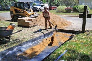 The trench for the sidewalk was lined with landscape fabric. Then 6 inches of base material was placed on it, topped with an inch of sand.