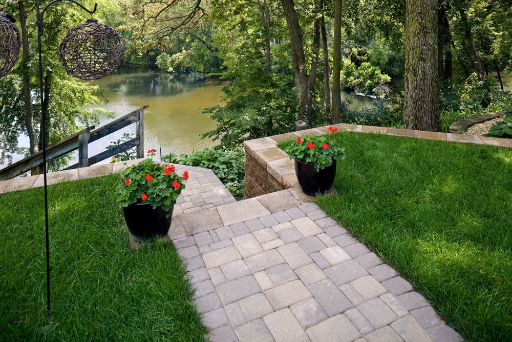 Paving stone walkway, retaining wall and steps leading down to a lake.
