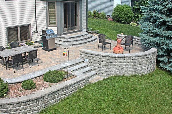 The versatility of concrete retaining wall units is on display here, with a curved freestanding wall, retainng wall planter beds, and stairs all in one great backyard living space..